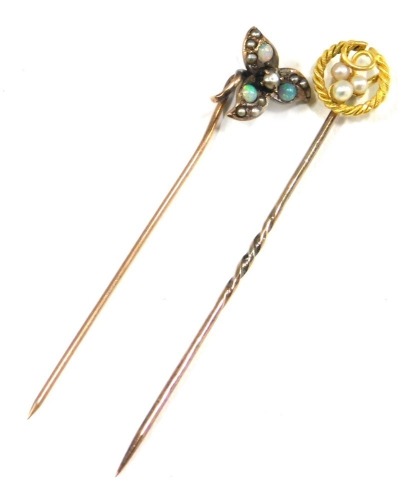 Two stick pins, comprising a stick pin set with opal and seed pearl with three leaf clover top, unmarked, 5cm high, and a stick pin with rope twist and seed pearl grape vine topped design, yellow metal stamped 15ct, 5.5cm high, 1.9g all in.