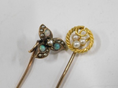 Two stick pins, comprising a stick pin set with opal and seed pearl with three leaf clover top, unmarked, 5cm high, and a stick pin with rope twist and seed pearl grape vine topped design, yellow metal stamped 15ct, 5.5cm high, 1.9g all in. - 2