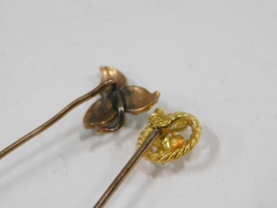 Two stick pins, comprising a stick pin set with opal and seed pearl with three leaf clover top, unmarked, 5cm high, and a stick pin with rope twist and seed pearl grape vine topped design, yellow metal stamped 15ct, 5.5cm high, 1.9g all in. - 3