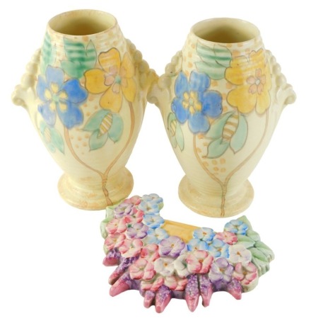 A pair of Kensington Art Deco vases, decorated with flowers, 23cm high, and a Beswick floral wall plaque, 20cm wide. (3)