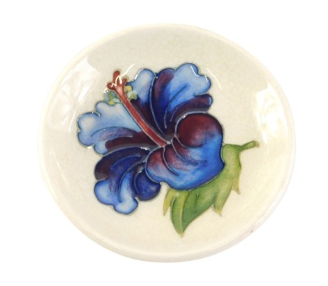 A Moorcroft pin dish, on a cream ground with central blue flower, stamp to underside, 8cm diameter.