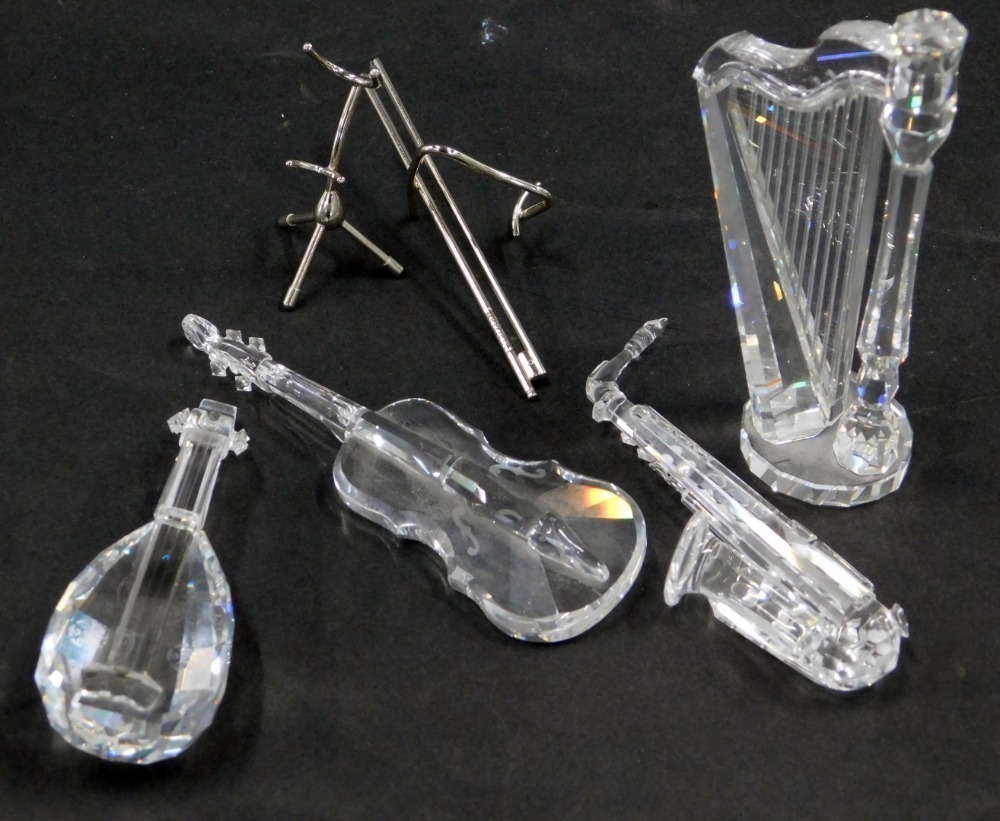 Four Swarovski crystal musical instruments, comprising harp, saxophone,  cello and violin, some with stainless steel stands,