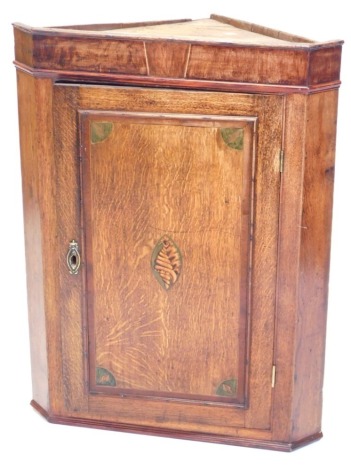 An early 19thC mahogany, oak and marquetry hanging corner cupboard, with single panelled door, 90cm high, 67cm wide.