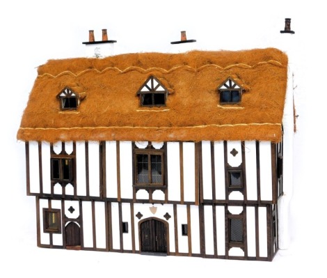 A three storey substantial Tudor style doll's house, with three chimneys, thatched roof, in painted Gothic style with panelled windows and doors and partially fitted interior, 103cm high, 120cm wide, 53cm deep. (AF)