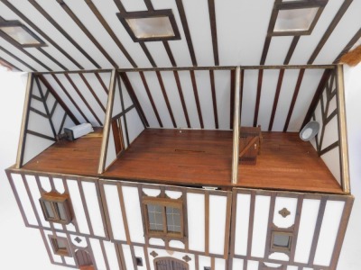 A three storey substantial Tudor style doll's house, with three chimneys, thatched roof, in painted Gothic style with panelled windows and doors and partially fitted interior, 103cm high, 120cm wide, 53cm deep. (AF) - 2