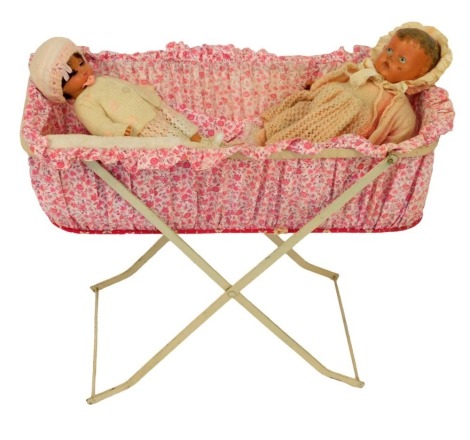 An early 20thC doll's crib, on a cream painted metal base, with floral surround, and two doll's, to include a plastic doll and a papier mache faced doll, each in knitted clothing.