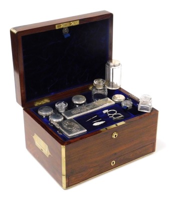 A Victorian rosewood and brass bound travelling box, the hinged lid opening to reveal a purple velvet fitted interior with a lift out tray containing cut glass and plate lidded bottles, boxes and jars, three manicure implements, with five recesses behind