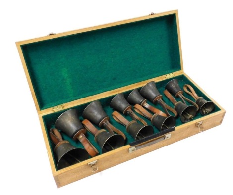 Twelve vintage graduated brass hand bells, with tan leather straps, denoting the note, cased.