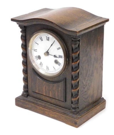 An early 20thC oak cased mantel clock, circular enamel dial bearing Roman numerals, eight day movement with coil strike, the case of architectural form, with spiral twist columns, raised on a plinth base, with pendulum, no key, 28cm high.