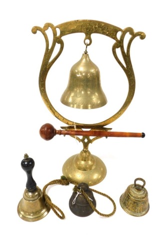 An early 20thC Indian brass table gong, with engraved floral and foliate decoration, 42cm high, a brass and wooden handled hand bell, and two further bells. (4)