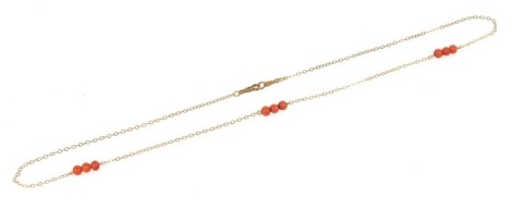 A 9ct gold cable link neck chain, set with three sets of three coral beads, at intervals, on a clip clasp, 1.7g all in.