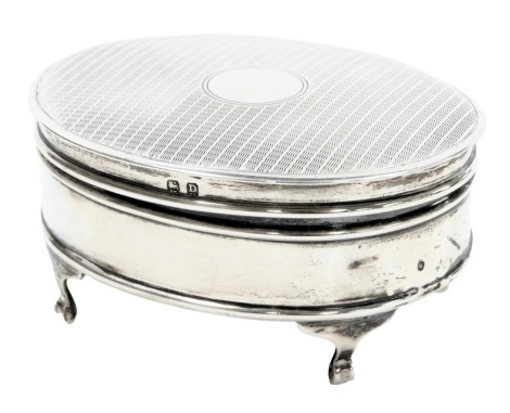 A George V silver oval dressing table box, with engine turned decoration, vacant circular reserve, raided on four scroll feet, Birmingham 1928, 4.33oz all in.