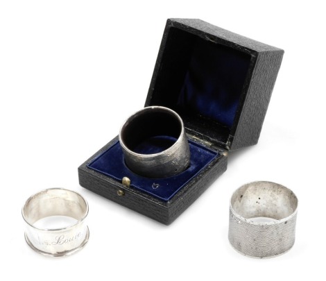 A George V silver napkin ring, with engine turned decoration, rectangular reserve, monogram engraved, Birmingham 1935, further napkin engraved Louie, Birmingham 1921, 1.47oz, and a silver overlaid wooden napkin ring, hallmarks worn, cased. (3)