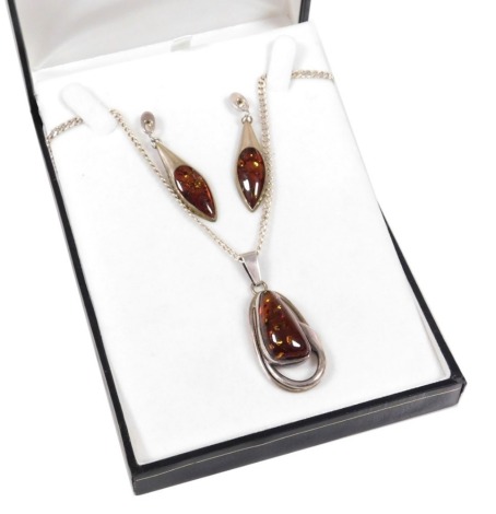 A silver and amber pendant, on a curb link neckchain with lobster claw clasp, together with a pair of amber earrings, set in white metal.