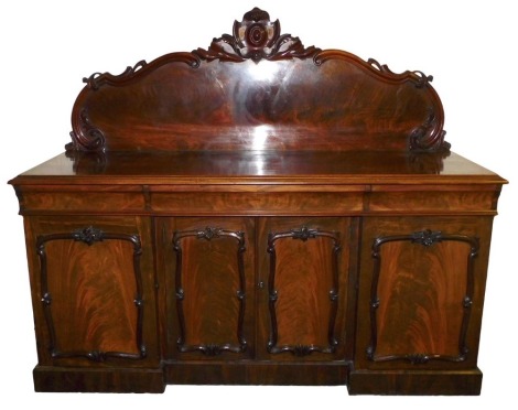 A Victorian mahogany break front sideboard, with a carved back over one long and two short cushion drawers, above a pair of central doors flanked by two further doors, the right enclosing a cellarette drawer, raised on a plinth base, 158cm high, 187cm wid