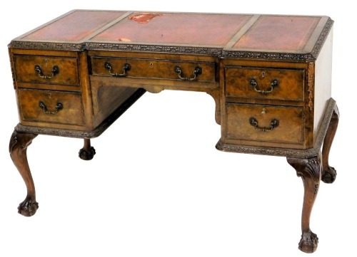 A walnut desk, the break front top with three red and gilt tooled leather insets, surrounded by a leaf carved border above an arrangement of five drawers, each with brass drop handles, on cabriole legs with ball and claw feet, 76cm high, 120cm wide, 61cm