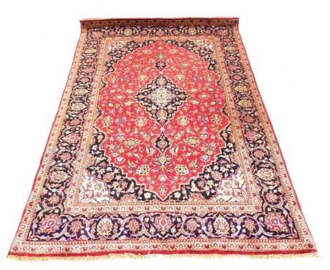 A Persian rug decorated with leaves and scrolls, on a red ground, with one wide and two narrow borders. PORTERS TO MEASURE.