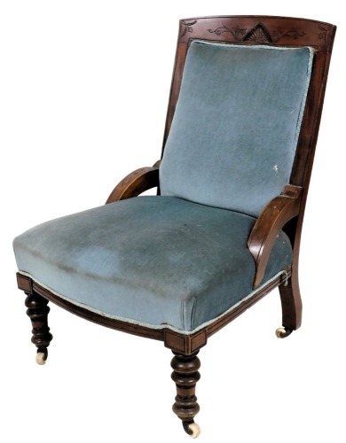 A late Victorian walnut nursing chair, with a blue upholstered padded back and seat, on turned legs with castors.