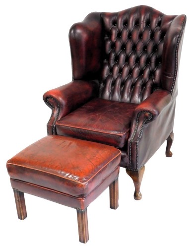 A oxblood red leather upholstered wing back Chesterfield armchair, in George III style with studded borders, on cabriole legs, an a similar stool. The upholstery in this lot does not comply with the 1988 (Fire & Fire Furnishing) Regulations, unless sold