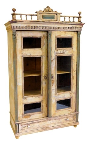 A 19thC continental painted cabinet, the cornice with spindle turned rails and a central tablet, above a carved frieze, two glazed doors and a frieze drawer, on bun feet, 208cm high, 122cm wide.