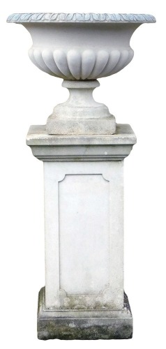 A reconstituted stone garden urn, of part fluted form, on a rectangular plinth with panelled sides, 115cm high.