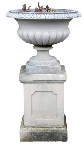 A reconstituted stone garden urn, of part fluted form, on a rectangular plinth with panelled sides, 90cm high, 53cm wide.