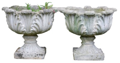 A pair of reconstituted stone garden urns, each cast with leaves, on a square base, 43cm high, 48cm wide.