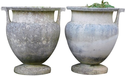 A pair of reconstituted stone two handled garden urns, of amphora style, on a circular plinth, 52cm high, 51cm wide. (AF)