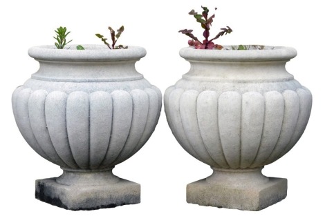 A pair of reconstituted part fluted vase shaped urns, each on a square base, 43cm high, 39cm wide.