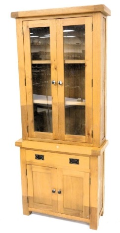 A light oak cabinet, the top with two glazed doors, the base with a drawer and two panelled doors, on stiles, 201cm high, 85cm wide.