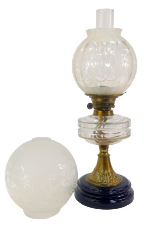 A late Victorian oil lamp, with clear glass central reservoir, on an embossed brass stem, raised on a black socle base, with chimney and associated shape, the oil lamp base 36cm high.