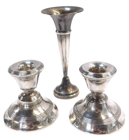 A pair of silver dwarf candlesticks, each of plain design, on a waisted foot, with rubbed hallmarks, 7cm high, and a silver plated stem vase, 13cm high. (3)