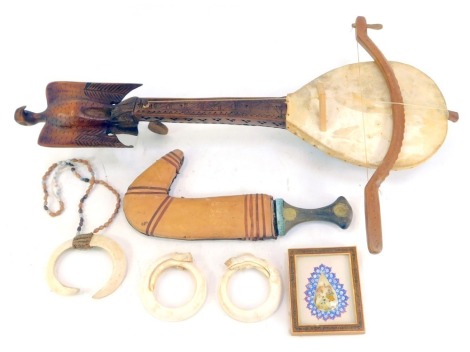 A Balkan gusle, the kalica covered with animal skin, the neck with carved decoration surmounted by an eagle, 65cm long, with bow, together with an Eastern dagger, animal horn bangles, and an Eastern framed mother of pearl token decorated with...