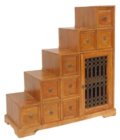 An Eastern mango wood cabinet, of stepped design, with an arrangement of nine drawers, with an open metalwork cabinet enclosing a single shelf, 108cm high, 100cm wide, 40cm deep.