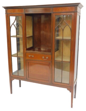 An Edwardian mahogany and boxwood inlaid cabinet, the top with a moulded cornice above a central recess with drawer above a cupboard inlaid with bows and swags, flanked with panelled glazed doors enclosing three shelves, with glass side panels,...