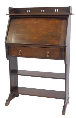 An early 20thC oak student's type bureau, the top with a moulded edge with raised carved pierced back, the fall enclosing a pen recess and arrangement of further recesses, the base with drawer with brass teardrop handles, above two open shelves,...