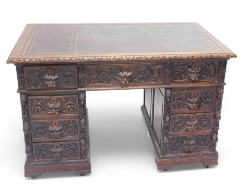 A late Victorian oak pedestal desk, carved with scrolls, leaves and masks, the rectangular top with an oxblood coloured leather inset, above an arrangement of nine drawers, on block feet with castors, 79cm high, 124cm wide.