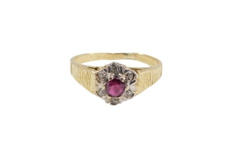 An 18ct gold ruby and diamond cluster ring, set with round brilliant cut ruby, in six claw setting, surrounded by tiny diamonds in white gold with bark effect shoulders, on a yellow metal band, ring size J½, 2.6g all in.