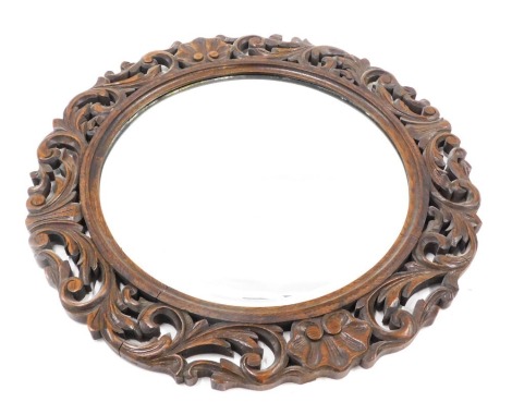 An oak wall mirror, with a foliate scroll carved border and a circular bevelled plate, 65cm diameter.