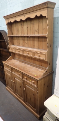 A rustic pine dresser, arched plate rack top above arrangement of four drawers, on sideboard base with three drawers and three cupboards, on plinth.