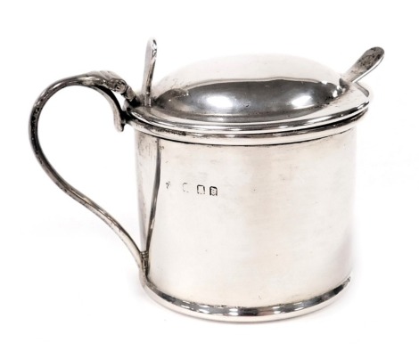 A George V silver drum mustard pot, of cylindrical form, with a hinged lid and blue glass liner, London 1919, together with a mustard spoon, 2.18oz.