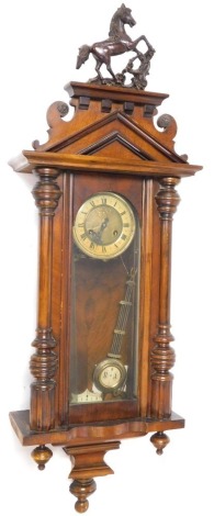 A late 19thC Continental walnut cased wall clock, circular brass dial with chapter ring bearing Roman numerals, eight day movement, the pediment surmounted by a prancing horse, the case with glazed door flanked by turned pilasters, with pendulum and key, 