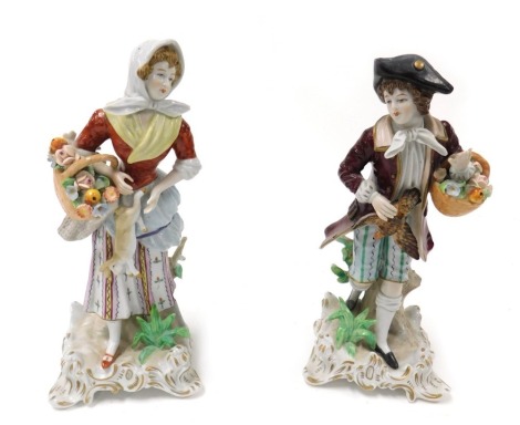 A pair of 20thC Sitzendorf porcelain figures, modelled as a gallant with game bird and basket of flowers, and a lady with a basket of fruit and flowers and a rabbit, each raised on a rococo scroll base, printed marks, 23cm high.