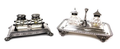 A Victorian silver plated desk stand, of rectangular form, with a gadrooned rim, enclosing two pen recesses, and a pair of cut glass inkwells, with hinged, plated lids, flanking a candlestick, raised on four scroll feet, 23cm wide, together with a further