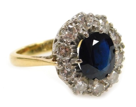 A sapphire and diamond ring, the oval cut sapphire in a surround of ten brilliant cut diamonds, in yellow metal stamped 18ct, diamonds approximately ¾ carat, size N, 5.4g.