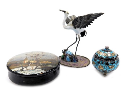 An early 20thC silver and enamel figure of a stork, modelled perched on a rock, 7cm high, continental white metal and champleve enamel cylindrical pot and cover, raised on three ball feet, and a Russian lacquer box and cover, painted with a winter landsca