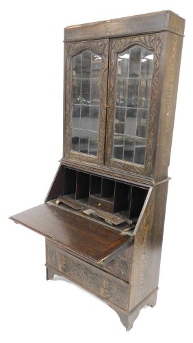 A 1920's oak bureau bookcase, with lion's mask handles, and profusely floral and foliate carved, the plain pediment over a pair of glazed doors, internal shelves lacking, above a fall flap opening to reveal a single drawer and six recesses, over three gra