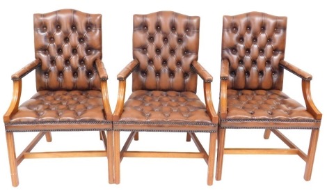 Three mahogany and tan leather armchairs, with button upholstered back, seat and arm rests, raised on square legs united by a H frame stretcher, 62cm wide.