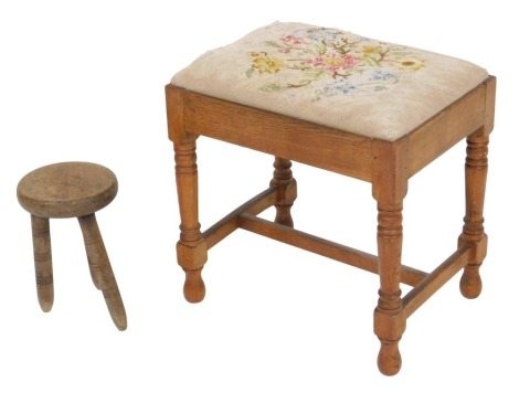 An early 20thC oak stool, with a wool work seat, raised on turned legs, 46cm wide, together with a milking stool, 26cm high. (2)