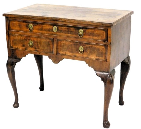 A walnut and feather banded lowboy, the rectangular quarter veneered top with a cross banded border and moulded edge, above arrangement of one long and two short drawers, with brass ring handles, on cabriole legs and pad feet, the drawer bearing label for